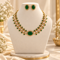 Green and gold necklace with matching stud earrings displayed on a cream jewellery bust