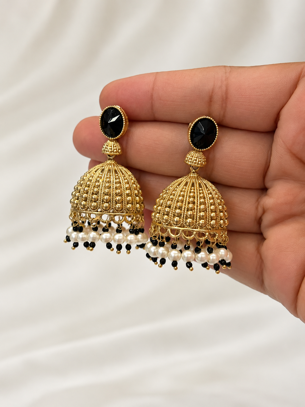 Natural-looking close-up of black and gold brass Jhumka earrings held by hand