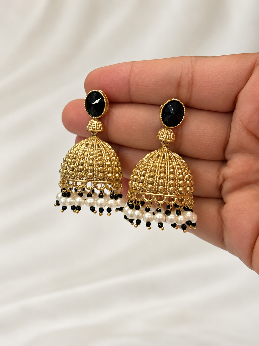Natural-looking close-up of black and gold brass Jhumka earrings held by hand